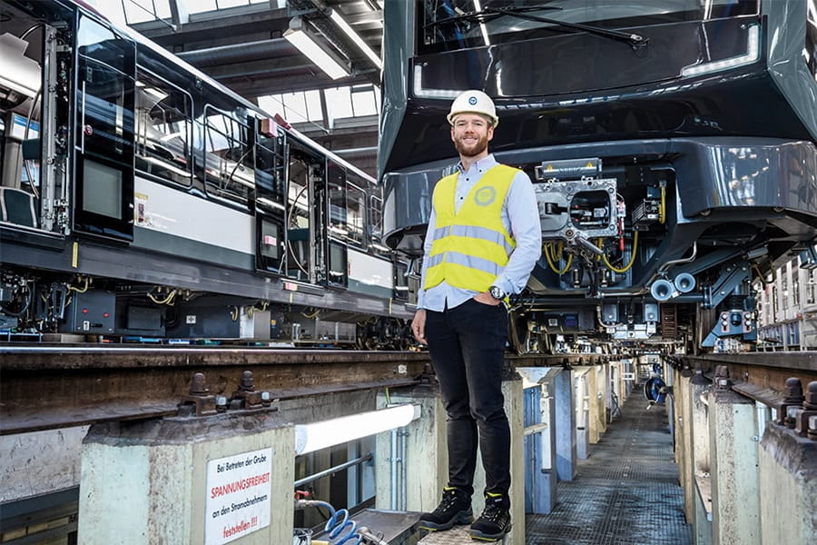 A TÜV SÜD expert in a safety vest and white helmet ensures quality and safety in a train maintenance facility.
