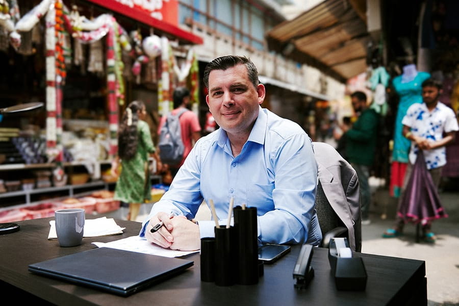 A man sits at a desk on a street in India.