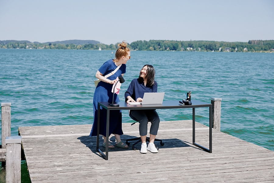 Two women have a laugh together on a pier at a Bavarian lake.