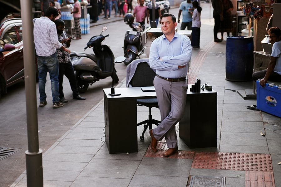A man stands in front of a desk on a busy street in India