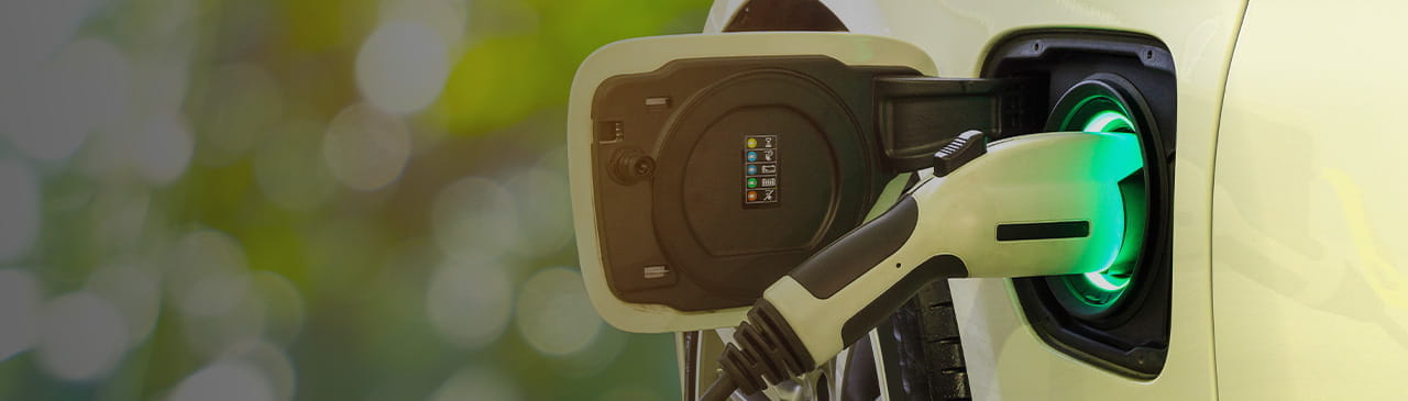 EV Car or Electric car at charging station with the power cable supply plugged in on blurred nature with soft light background.